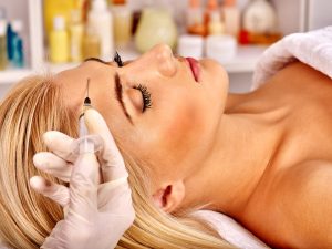 Beauty woman giving botox injections on forehead.
