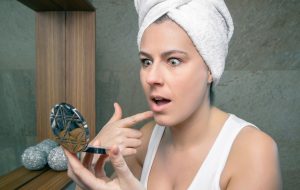 Surprised woman looking an acne pimple in mirror