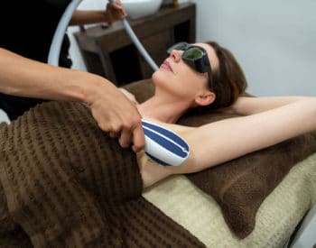 woman laying down wearing goggles receiving sciton laser hair removal on armpit